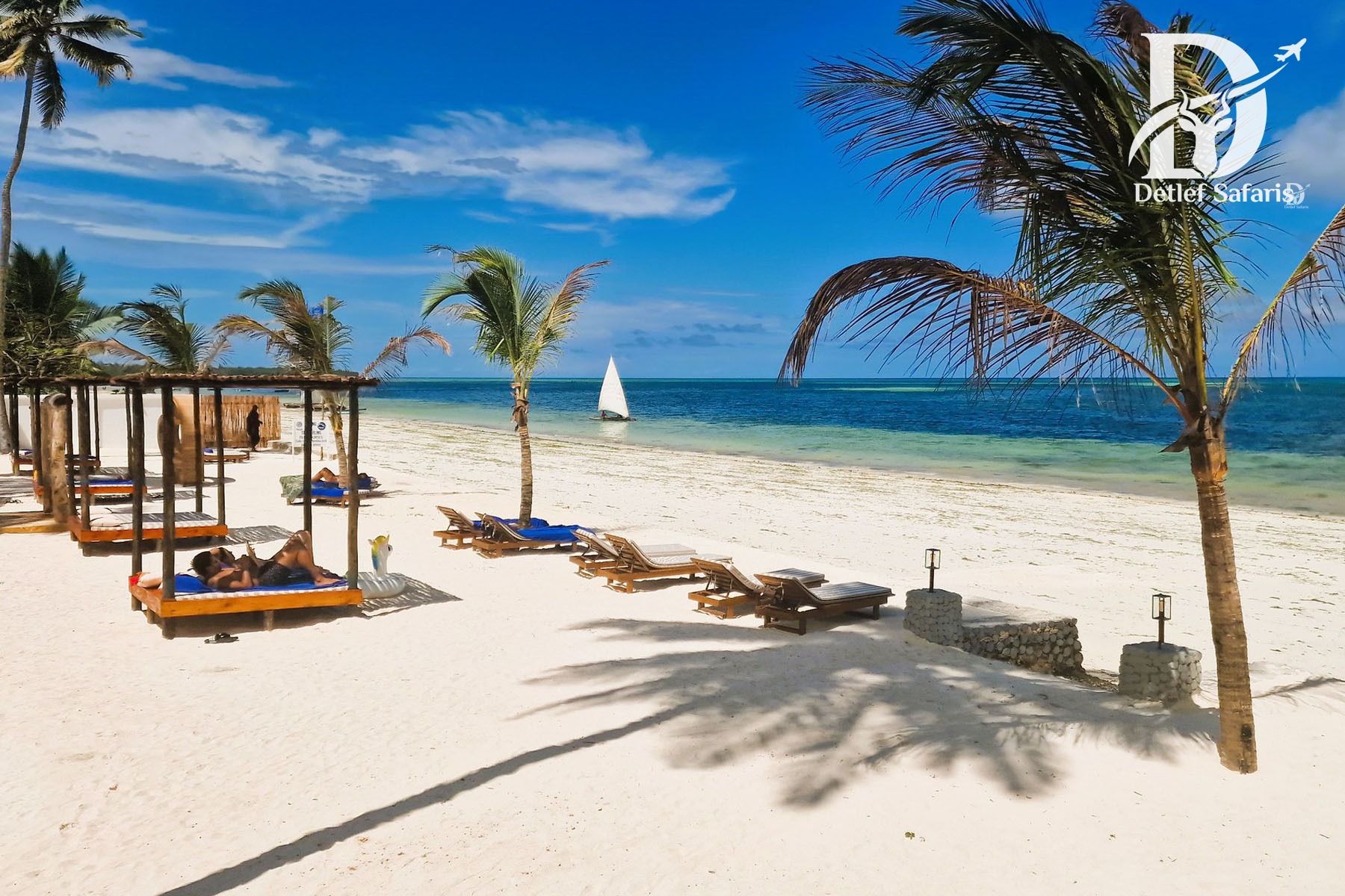 Beach loungers and a dhow sailboat on Zanzibar’s turquoise coastline